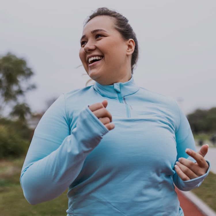 Smiling woman in a pale blue running top jogging on an outdoor path
